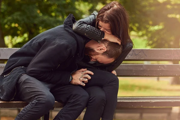 Atractiva pareja moderna sentada en un banco en un parque . — Foto de Stock