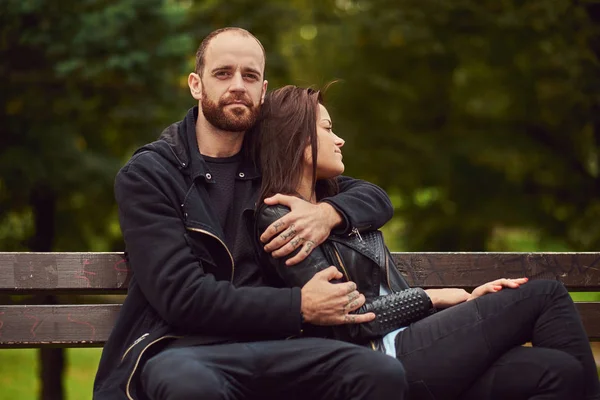 Attraente coppia moderna seduta su una panchina in un parco . — Foto Stock
