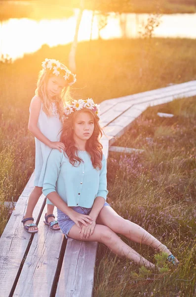 Două surori frumoase care stau pe fundalul unui peisaj frumos, merg pe câmp lângă un iaz la apusul soarelui . — Fotografie, imagine de stoc