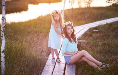 Güzel bir manzara arka plan karşı duran iki güzel kız yürümek bir gölet yakınındaki sahada günbatımında.