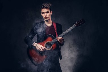 Bir akustik gitar çalmaya şık giysiler içinde şık saç ile şık genç müzisyen.