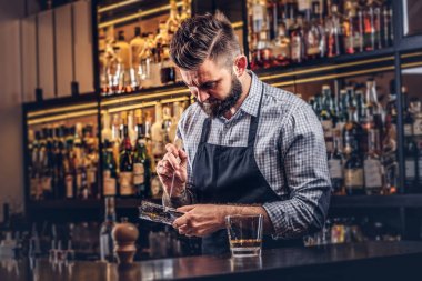 Buz bir kokteyl bar counter arka plan yapmak için bir gömlek ve önlük şık sakallı barmen böler.