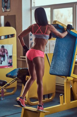 Güzel seksi atletik genç esmer çalışma dışarı, spor salonunda basın makine ile buzağı ayak kasları egzersiz bir spor giyim.