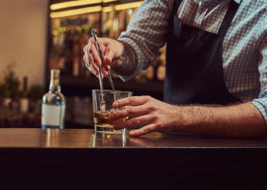 Bir gömlek ve önlük şık acımasız barmen, bir kokteyl bar counter arka plan yapar.
