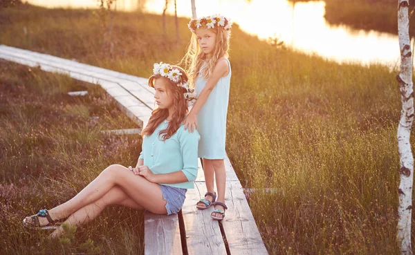 Dos hermosas hermanas de pie sobre el fondo de un hermoso paisaje, caminar en el campo cerca de un estanque al atardecer . —  Fotos de Stock