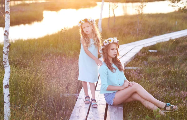 Dos hermosas hermanas de pie sobre el fondo de un hermoso paisaje, caminar en el campo cerca de un estanque al atardecer . —  Fotos de Stock