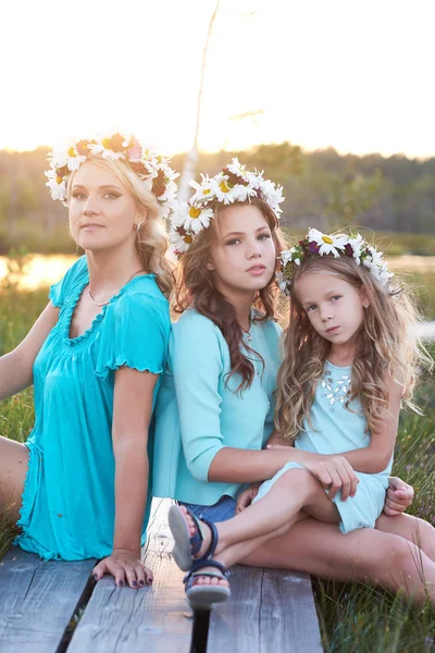 Mother and her daughters relaxing outdoors while sitting on a wooden path in a field at sunset. — Stock Photo, Image