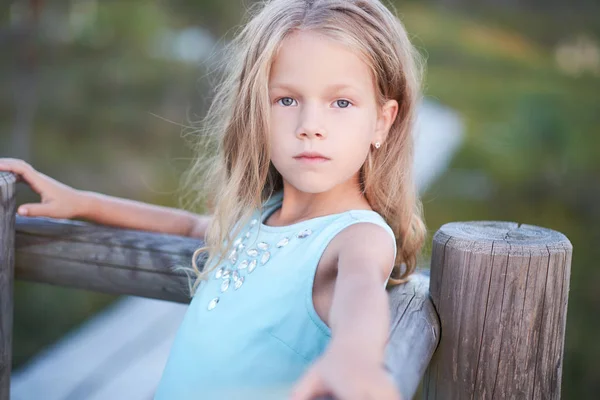 Porträt eines niedlichen kleinen Mädchens, das im Freien steht, während es sich an einen Holzzaun lehnt. — Stockfoto