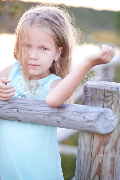 Portret Ładna dziewczynka, stojący na zewnątrz, podczas gdy pochylony na drewnianym płotem. — Zdjęcie stockowe