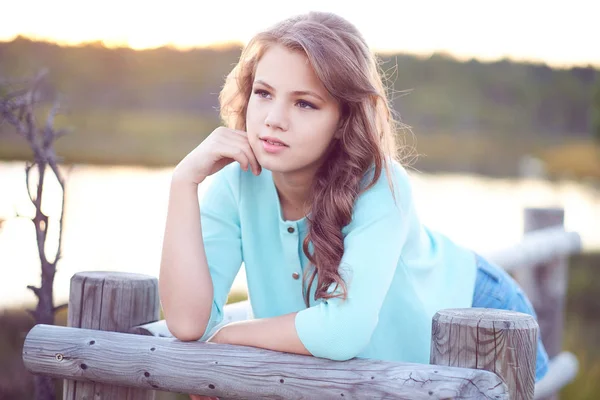 Porträt eines schönen Mädchens, das im Freien steht und sich an einen Holzzaun lehnt. — Stockfoto