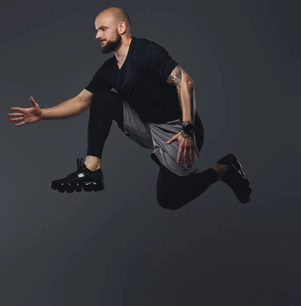 Handsome bearded athlete in sportswear jumping in a studio.