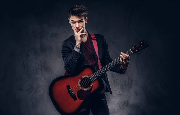 Przystojny młody muzyk przemyślany z stylowe włosów w eleganckie ubrania pozowanie z gitarą w rękach. — Zdjęcie stockowe