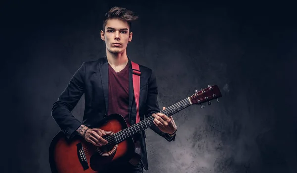 Stijlvolle jonge muzikant met stijlvolle haren in elegante kleding, spelen op een akoestische gitaar. — Stockfoto