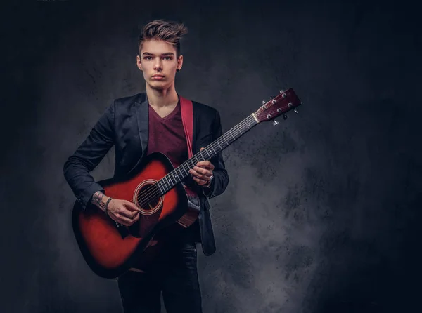 Elegante joven músico con el pelo elegante en ropa elegante, tocando en una guitarra acústica . — Foto de Stock