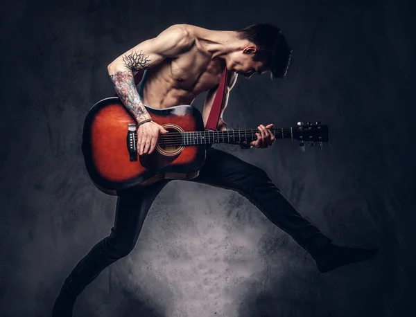 Stiliga shirtless unga musiker spelar gitarr medan hoppning. — Stockfoto