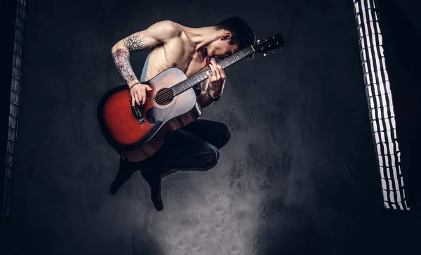 Guapo sin camisa joven músico tocando la guitarra mientras salta . — Foto de Stock