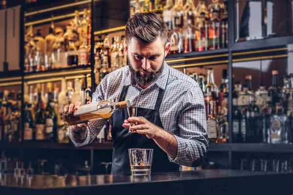 Elegante barman brutale in camicia e grembiule fa un cocktail al bancone del bar sfondo . — Foto Stock