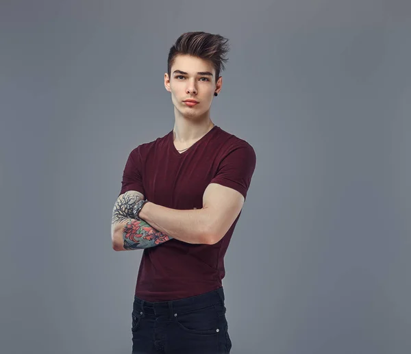 Bello ragazzo alla moda con capelli alla moda e tatuaggio sul braccio in posa in uno studio . — Foto Stock