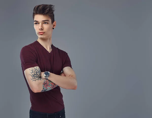 Guapo joven de moda con el pelo elegante y tatuaje en su brazo posando en un estudio . —  Fotos de Stock