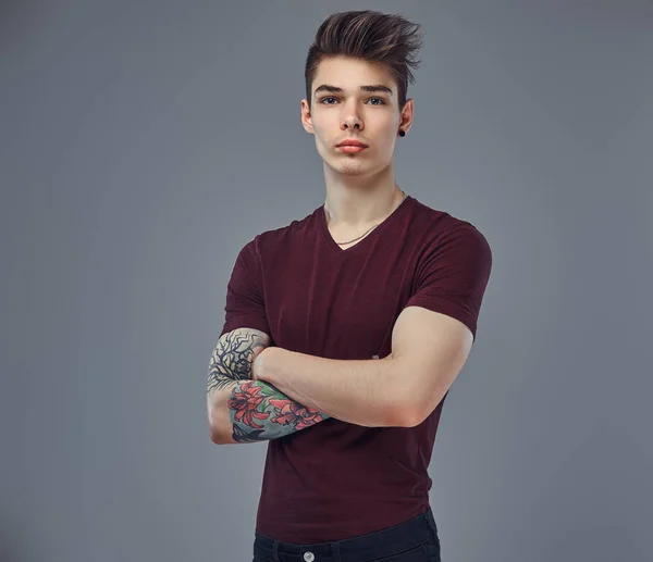 Schöner modischer junger Kerl mit stylischem Haar und Tätowierung auf dem Arm posiert in einem Studio. — Stockfoto