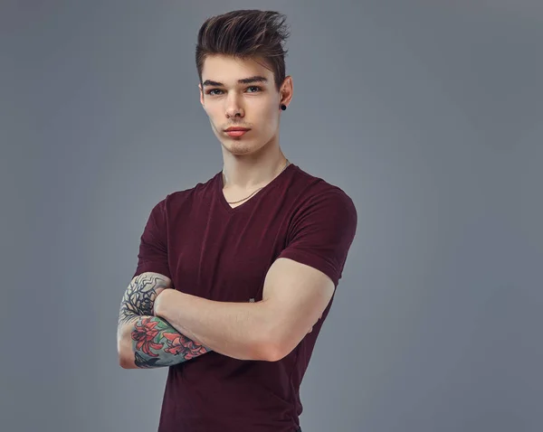 Knappe modieuze jonge kerel met stijlvolle haar en tattoo op zijn arm poseren in een studio. — Stockfoto