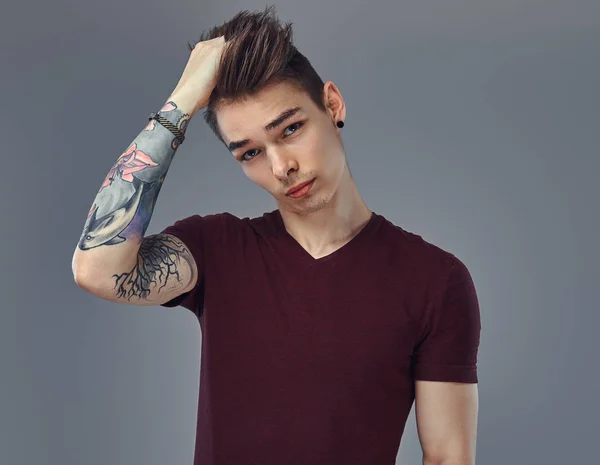 Bello ragazzo alla moda con capelli alla moda e tatuaggio sul braccio in posa in uno studio . — Foto Stock