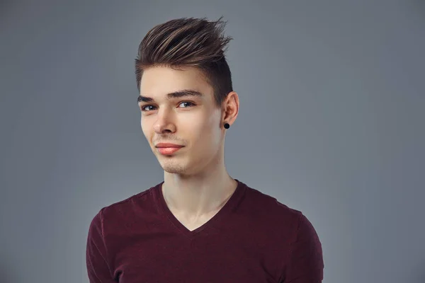 Schöner modischer junger Kerl mit stylischem Haar und Tätowierung auf dem Arm posiert in einem Studio. — Stockfoto