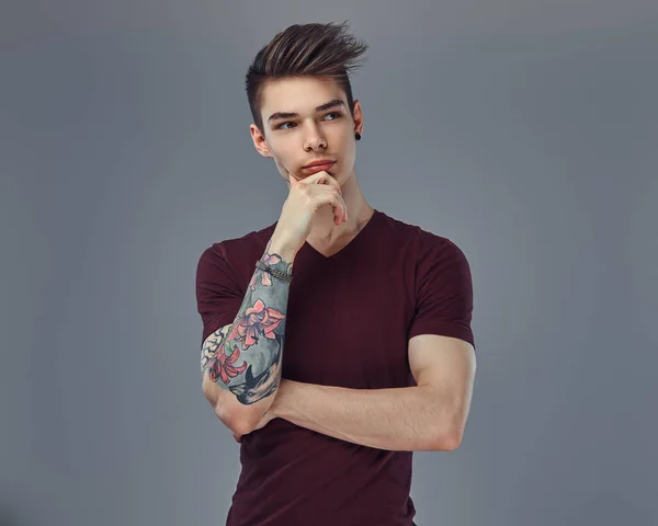 Bello ragazzo alla moda con capelli alla moda e tatuaggio sul braccio in posa in uno studio . — Foto Stock