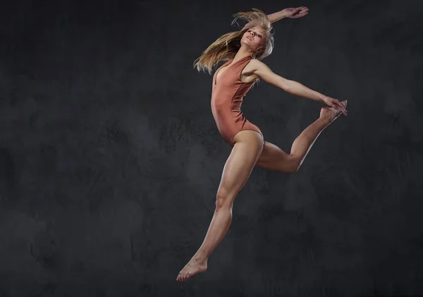 Die junge grazile Ballerina tanzt und springt in einem Studio. isoliert auf dunklem Hintergrund. — Stockfoto