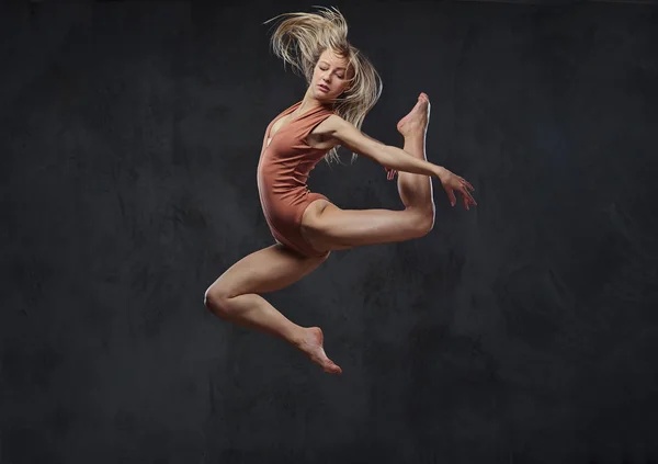 Die junge grazile Ballerina tanzt und springt in einem Studio. isoliert auf dunklem Hintergrund. — Stockfoto