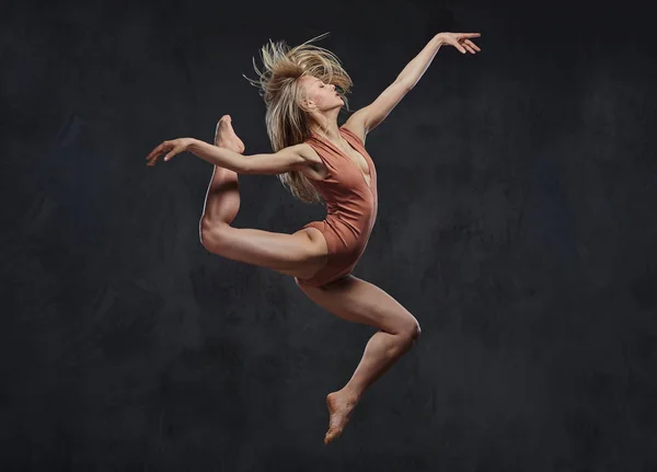 Die junge grazile Ballerina tanzt und springt in einem Studio. isoliert auf dunklem Hintergrund. — Stockfoto