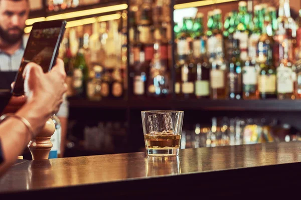 Abgeschnittenes Bild eines Kunden der Bar, der am Telefon ein Foto von einem Glas Alkohol auf einem Tresen macht. — Stockfoto