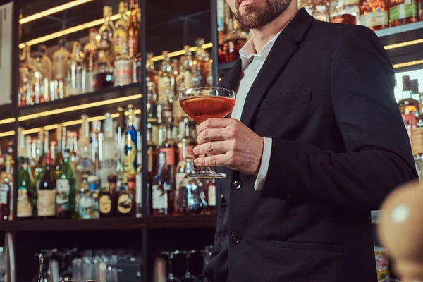 Bonito macho elegante detém um copo de álcool exclusivo em pé no bar contador de fundo . — Fotografia de Stock