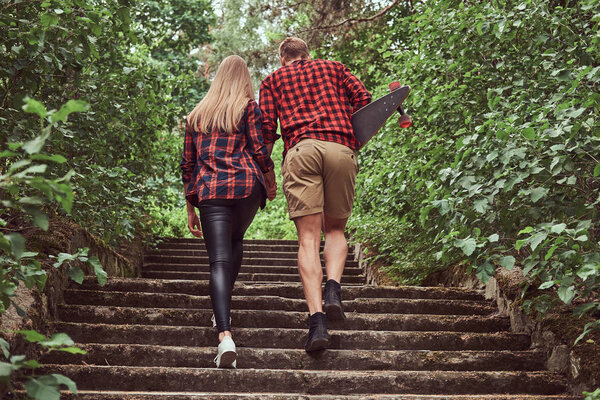 Young hipster couple, walk in a park, holding hands, climbing up the stairs.