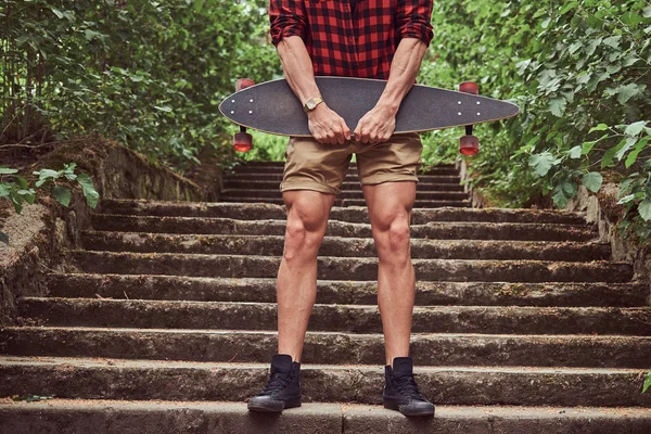 Immagine ritagliata di un pattinatore muscoloso, in piedi su gradini, tiene lo skateboard . — Foto Stock