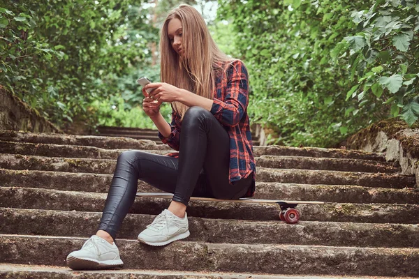 Dziewczyna Młoda Blondynka hipster za pomocą smartfona siedząc na schodach w parku. — Zdjęcie stockowe