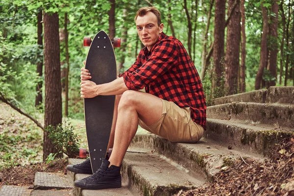 Mladý pohledný bokovky člověk odpočívá v parku, po jízdě na skateboardu. — Stock fotografie