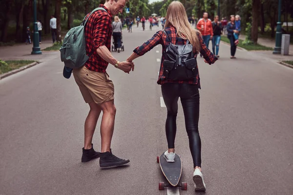 Jovem casal hipster. Guy ensina sua namorada a andar de skate na rua em um parque . — Fotografia de Stock