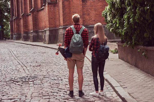 Jovem casal hipster, bonito patinador e sua namorada andando em torno de uma antiga ruas da Europa . — Fotografia de Stock