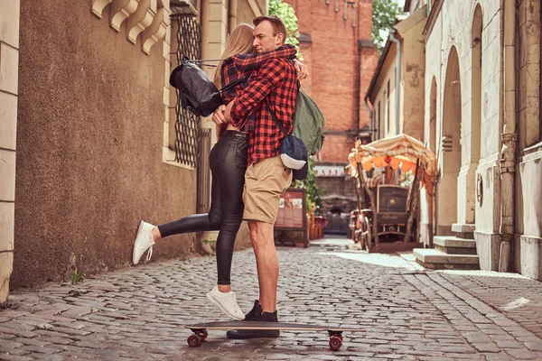 Unga hipster par, stilig skater och hans flickvän Gos stående på de gamla smala gatorna i Europa. — Stockfoto