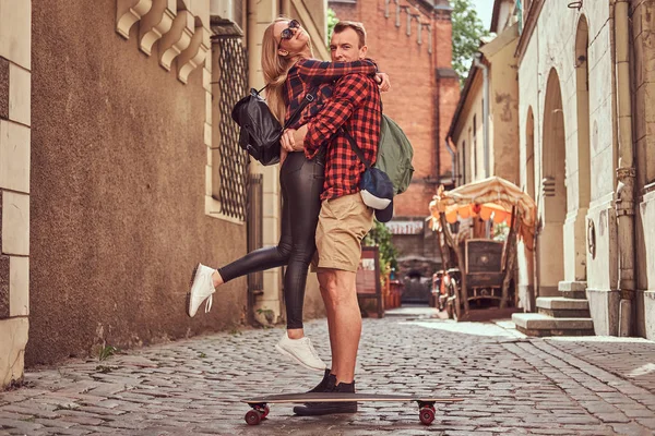 Unga hipster par, stilig skater och hans flickvän Gos stående på de gamla smala gatorna i Europa. — Stockfoto