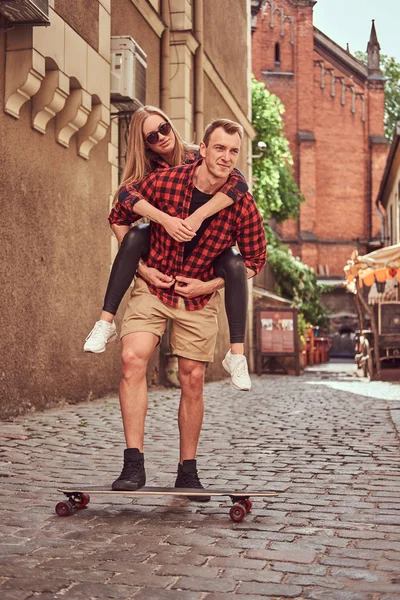 Unga hipster par, stilig skater och hans flickvän ha kul medan du går på den gamla smala gatan i Europa. — Stockfoto