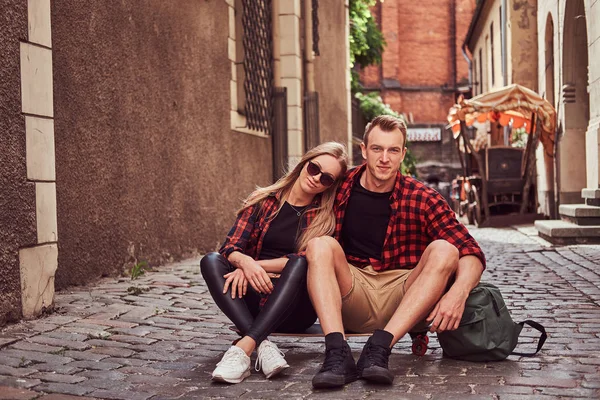 Jonge gelukkig hipster paar, rust tijdens een wandeling zitten op de stoep in de oude straat van Europa. — Stockfoto