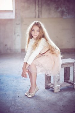 Bir stüdyoda bir tahta sandalyede oturan sevimli küçük kız modeli.