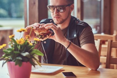 Bir hamburger yeme bir şık saç ve sakal ile yakışıklı hipster yol kenarına yerleştirilen bir kafede yemek yemeye karar verdim bir masada oturur.