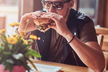 Bir hamburger yeme bir şık saç ve sakal ile yakışıklı hipster yol kenarına yerleştirilen bir kafede yemek yemeye karar verdim bir masada oturur.