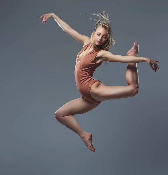 Joven bailarina elegante baila y salta en un estudio. Aislado sobre un fondo gris . — Foto de Stock