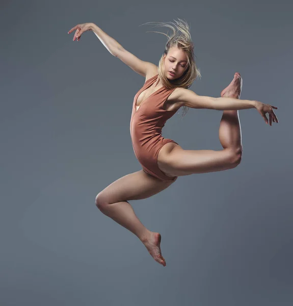 Jovem bailarina graciosa dança e salta em um estúdio. Isolado em um fundo cinza . — Fotografia de Stock