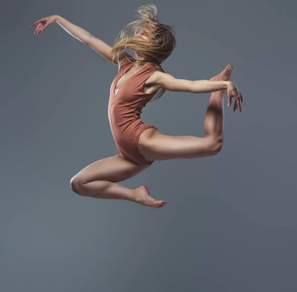 Jovem bailarina graciosa dança e salta em um estúdio. Isolado em um fundo cinza . — Fotografia de Stock