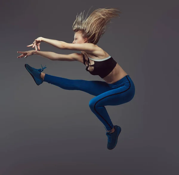 Joven bailarina en ropa deportiva baila y salta en un estudio. Aislado sobre un fondo gris . —  Fotos de Stock